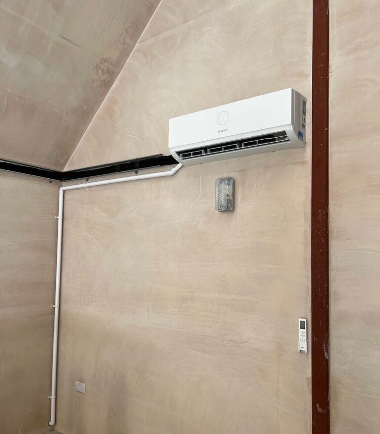 Bosch wall-mounted air conditioning unit installed high on a beige workshop wall with neatly routed services and controller