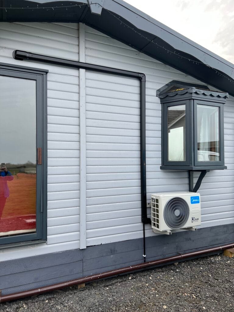 Midea outdoor air conditioning unit with black trunking on a timber lodge