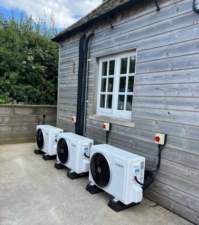 Three Bosch outdoor air conditioning units installed in a row beside a timber outbuilding