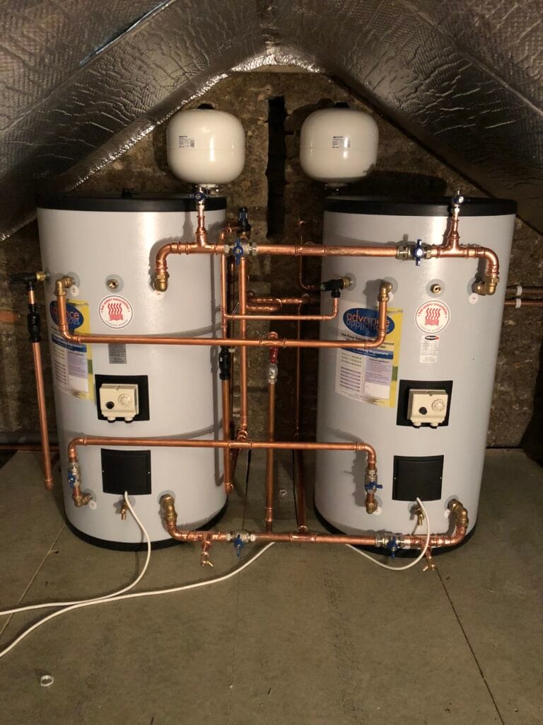 Twin hot water cylinders with expansion vessels and carefully arranged copper pipework installed in an attic plant space